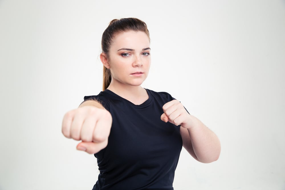 Portrait of a fat woman in sports wear hitting at camera isolated on a white background